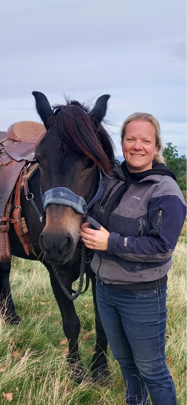 Marie Skramstad sammen med en oppsalet mørk hest ute på jordet