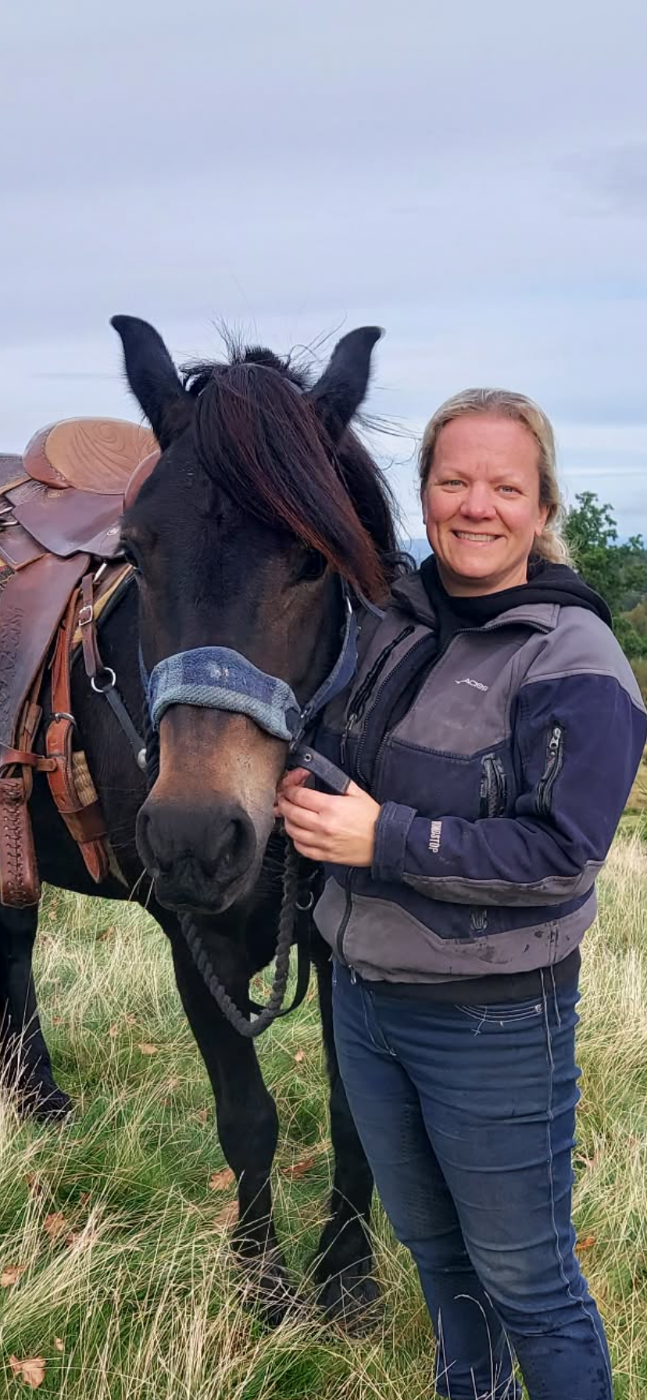 Marie Skramstad sammen med en oppsalet mørk hest ute på jordet